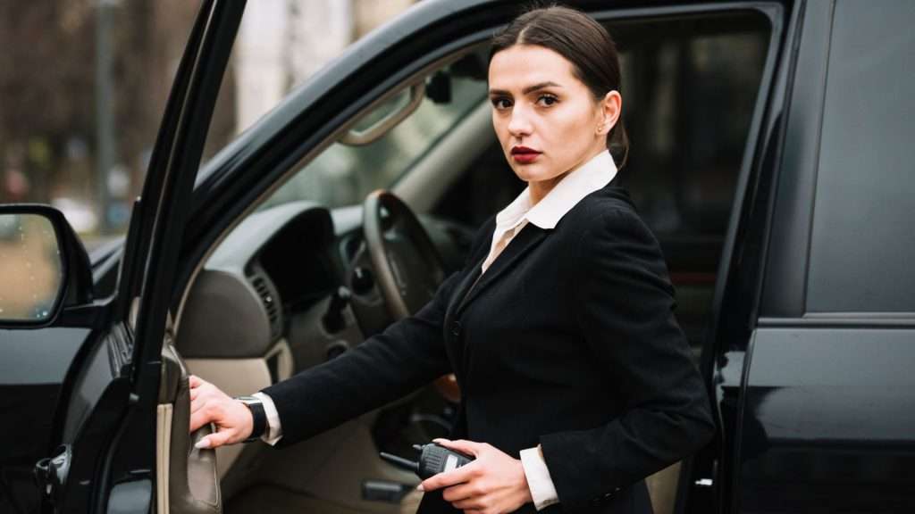 Female chauffeur standing confidently next to luxury car on Gold Coast street.